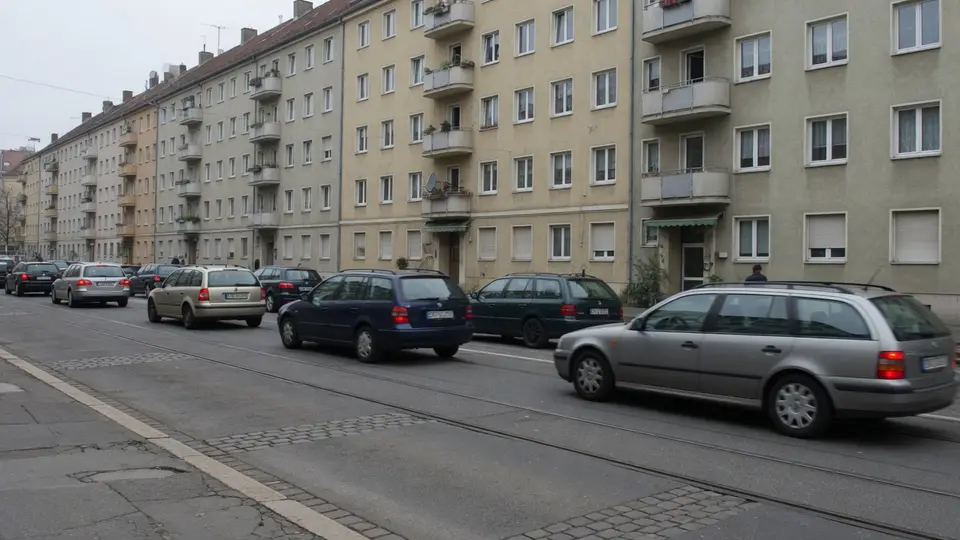 Parkende Autos an einer Wohnstraße mit Straßenbahnschienen, dahinter Wohnblocks aus der Nachkriegszeit.