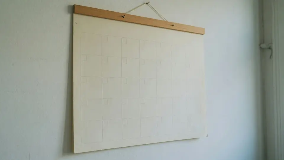 Ein leerer Wandkalender mit unbeschriftetem Monatsraster hängt an einer weißen Wand.