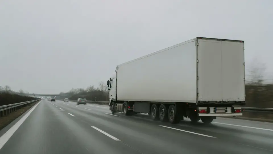 Ein Sattelzug mit weißem Kofferauflieger auf der Autobahn bei grauem Wetter, gesehen aus einem folgenden Fahrzeug.